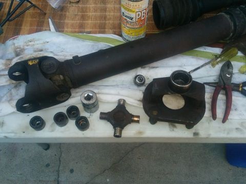1988 Ford Bronco - A disassembled driveshaft and universal joint components are laid out on a white cloth on a table, with a can of PB Blaster in the backgrou…