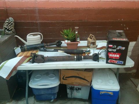 1988 Ford Bronco - Two driveshafts are laid out on a table covered with a patterned cloth, next to a white watering can and a toolbox covered in stickers. The…