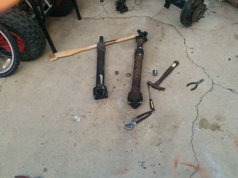 1988 Ford Bronco - Two driveshafts and various tools are laid out on a concrete surface next to a tire and wheel assembly. The scene appears to be a garage or…