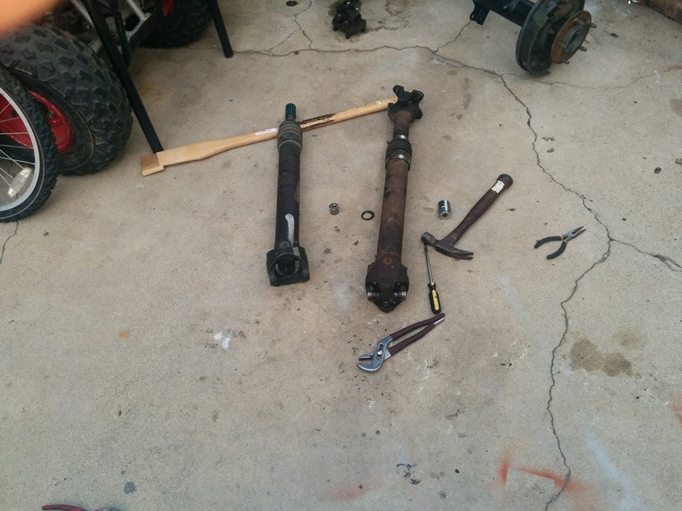Two driveshafts and tools on concrete floor.