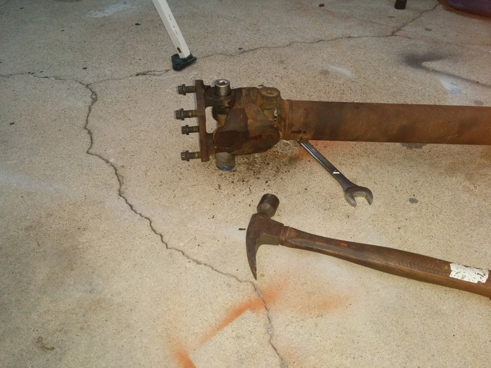 Rusty driveshaft on concrete floor with hammer and wrench