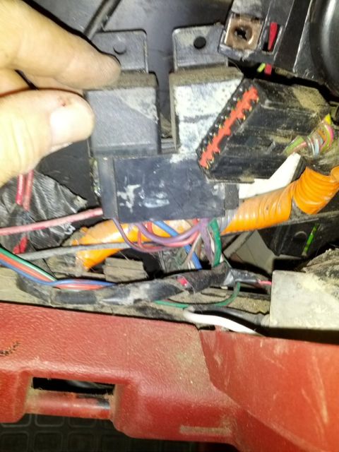 1992 Ford F-150 - A hand inspects a cluster of dusty electrical relays and a complex wiring harness within a vehicle's dashboard.