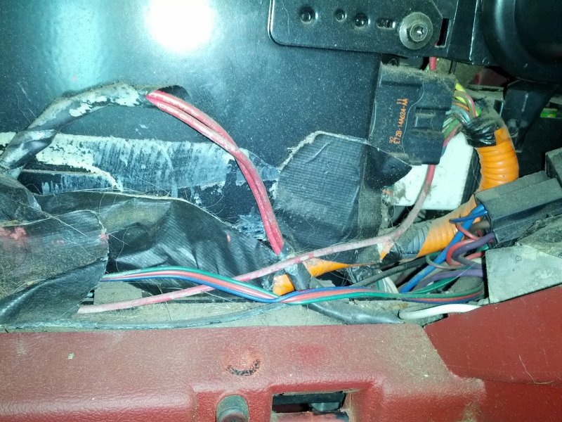 Tangled wires and electrical connectors under a vehicle dashboard.