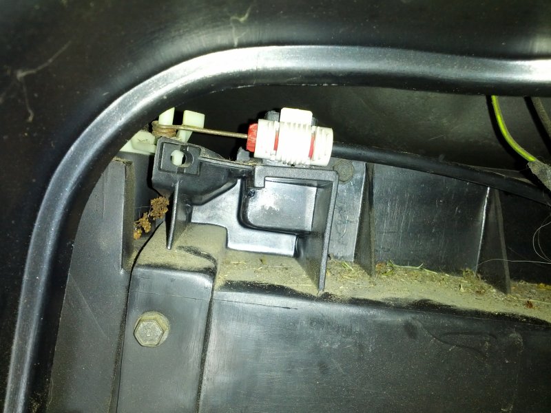 Close-up of a car's HVAC vent assembly with a cable actuator and debris.