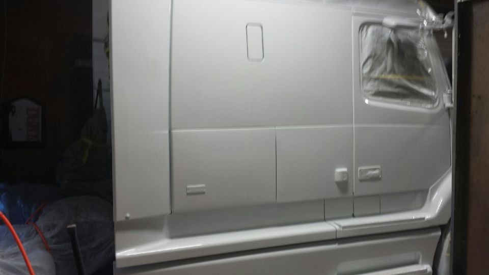White truck cab side view, window covered in plastic, in a workshop.