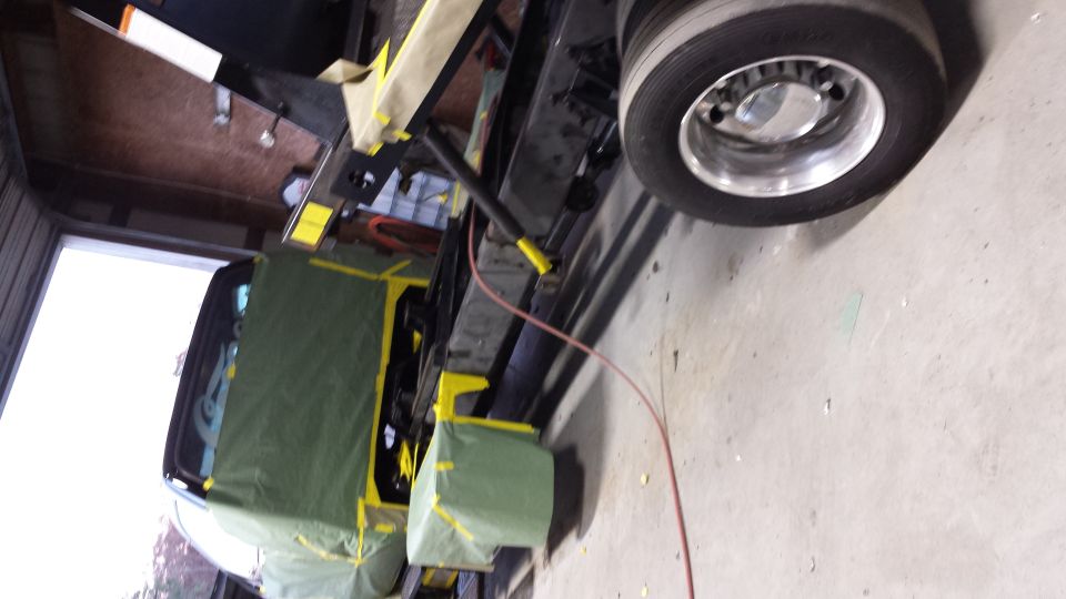 Ford F-650 truck in garage, prepped for paint with tarps and tape, front wheel visible.