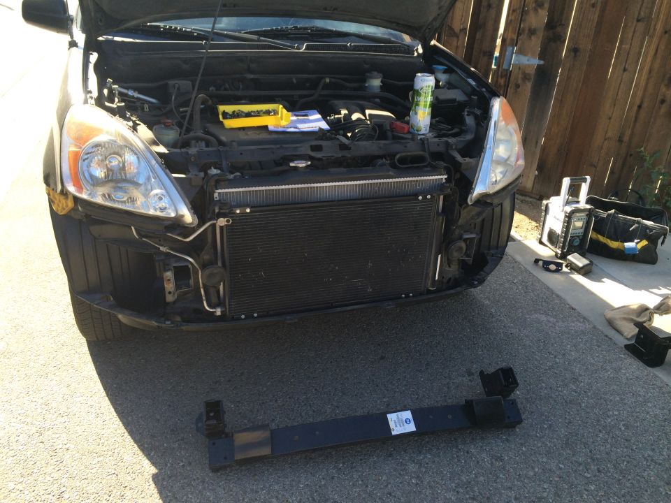 Dark SUV front end with hood open, new radiator visible, black bumper on ground.