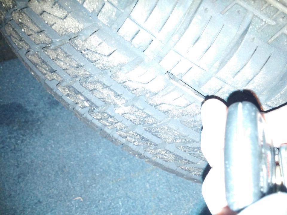 Photo of a tire tread beside a jack or tool at night