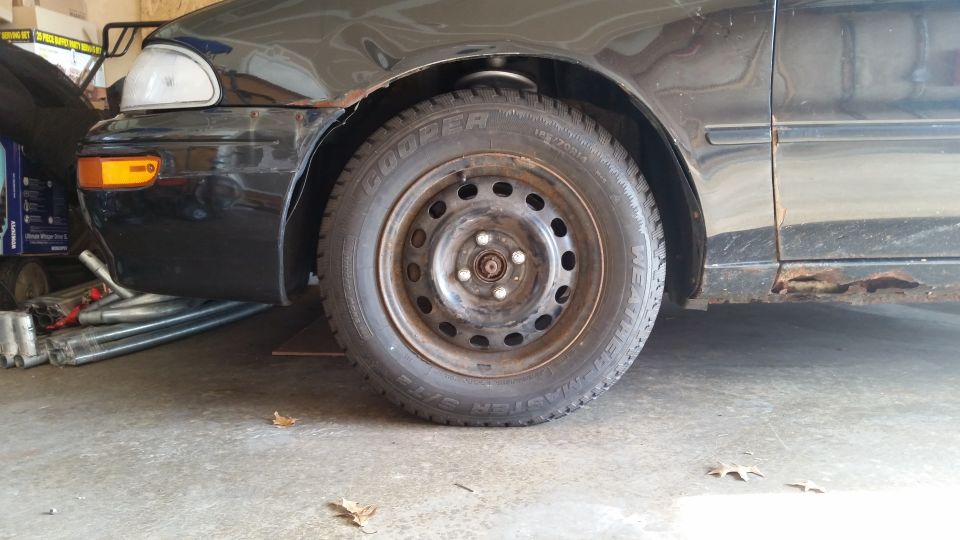 Black 1995 Geo Metro driver's side front wheel and fender with rust on the rocker panel.