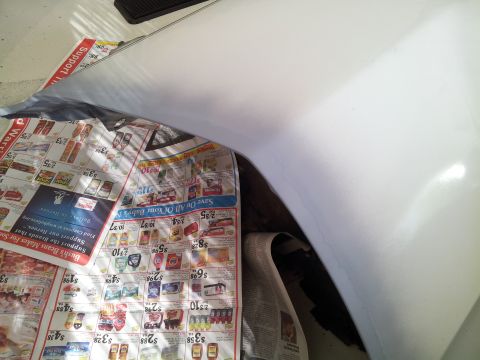 1976 Ford Ranchero - A white car fender is shown resting on a spread of newspapers. The fender appears to be undergoing some sort of repair or detailing process.