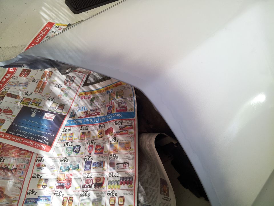 Close-up of a white car fender over newspapers.