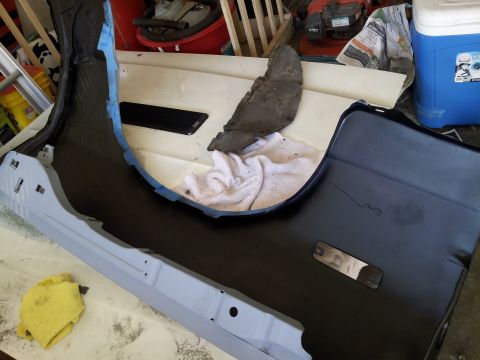 1976 Ford Ranchero - A black car bumper is laid out on a white surface, with blue painter's tape along its edge. A light gray metal part, possibly a frame compo…