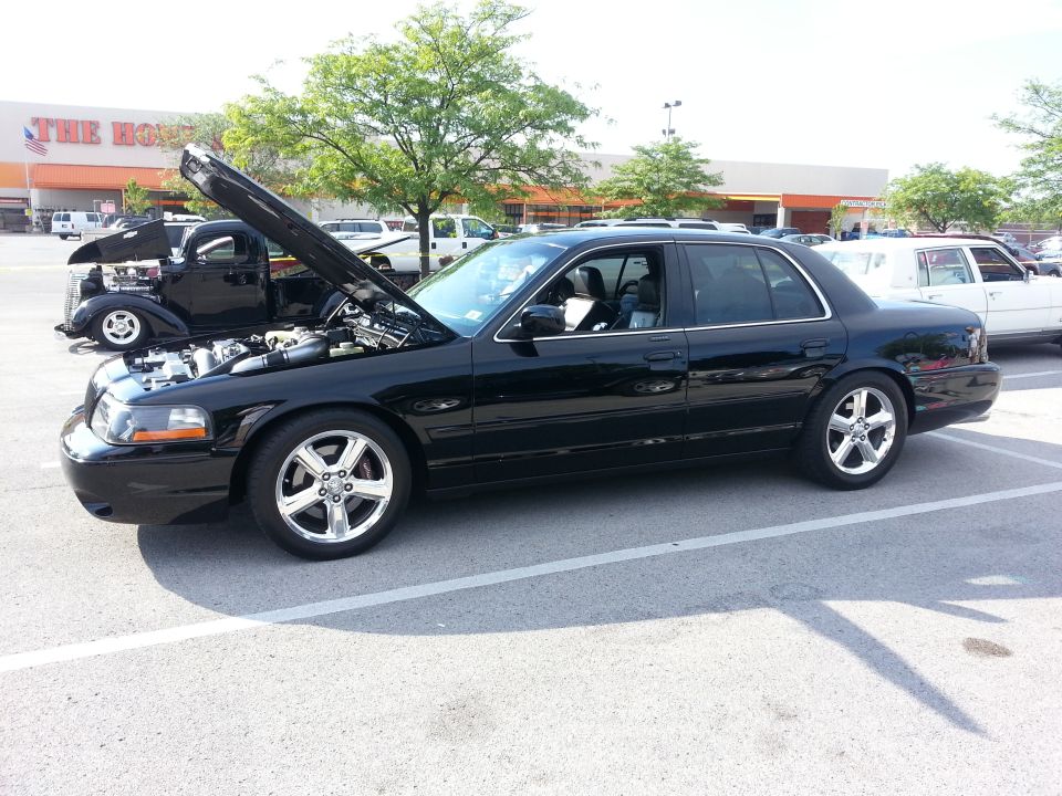 Black Mercury sedan with hood open, chrome wheels, parked in front of a store.