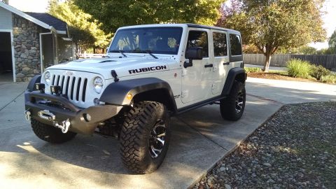 White four-door Jeep Wrangler Rubicon with aftermarket bumper and winch parked on a driveway.