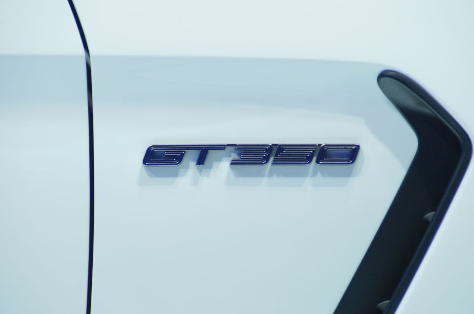 Close-up of a blue and silver GT350 badge on a white car near a black vent.
