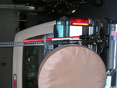 1996 Ford Bronco - A Hi-Lift Jack is mounted to the rear of a teal and white SUV, obscuring a tan spare tire cover.