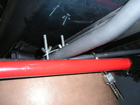 1996 Ford Bronco - A Hi-Lift Jack is secured beneath a vehicle, attached with bolts and wing nuts to a red bar and a gray hose.