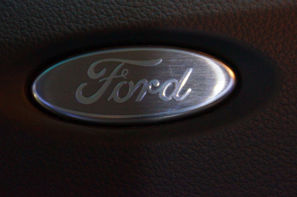 Brushed metal Ford emblem on a dark textured surface.