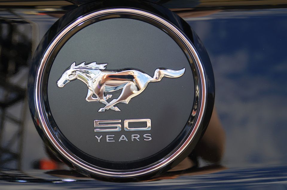 Chrome Mustang emblem with 50 YEARS text on a dark car.