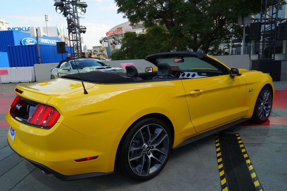 Yellow Ford Mustang convertible parked outdoors, rear passenger side view.