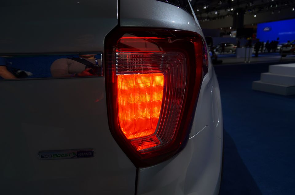 Silver SUV's illuminated red taillight with chrome trim reflecting a person.