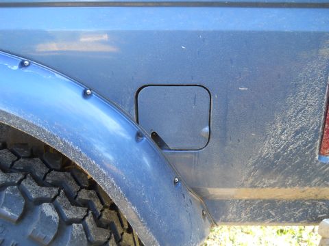 1992 Ford Bronco - A close-up view of the fuel filler door on a blue vehicle, likely a 1992 Ford Bronco, showing the textured tire and fender flare. The vehic…