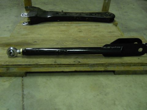 1992 Ford Bronco - Two black suspension control arms are displayed on a wooden pallet. The arm in the foreground has a spherical joint on the left end and a b…