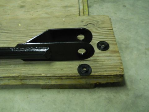 1992 Ford Bronco - A black metal bracket with two holes is shown resting on a wooden surface. Two black washers are also visible on the wood next to the brack…