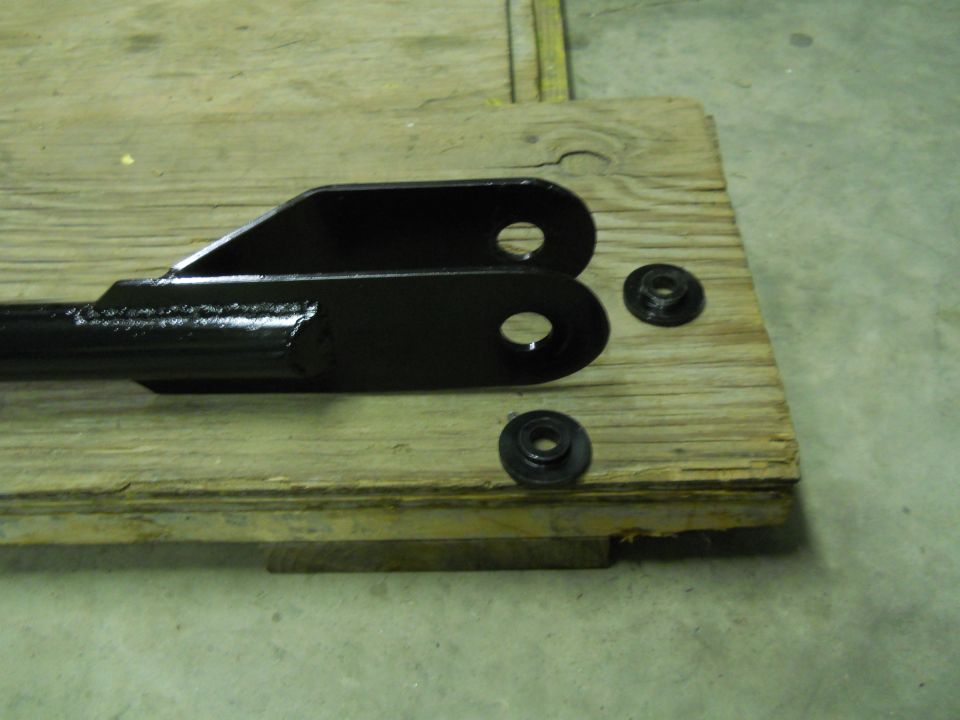 Black metal bracket with two holes and two washers on a wooden surface.