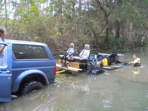 1992 Ford Bronco - A blue Ford Bronco is partially submerged in murky water next to a homemade watercraft with two seats and an engine. A man in a yellow vest…