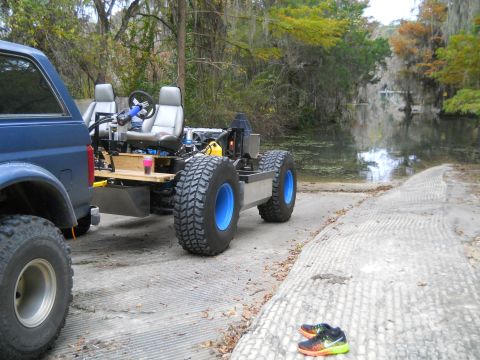 1992 Ford Bronco - A custom-built, open-air vehicle with two seats and large blue-rimmed tires sits on a boat ramp next to a blue Ford Bronco. The vehicle is…