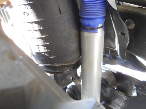 1992 Ford Bronco - A close-up view shows a silver shock absorber with a blue bellows boot, secured by a black zip tie, next to a black rubber air spring. The…