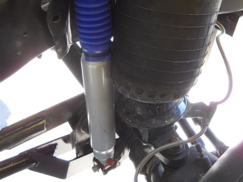 1992 Ford Bronco - A close-up view of the suspension system on a vehicle, showing a silver shock absorber with a blue bellows and a large black air spring. Me…