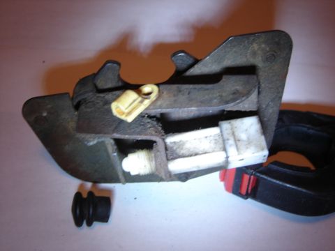 1996 Ford Bronco - Close-up of a removed tailgate latch assembly laid on a light surface, showing the greasy steel latch plate, jaw and pawl, a brass rod clip…