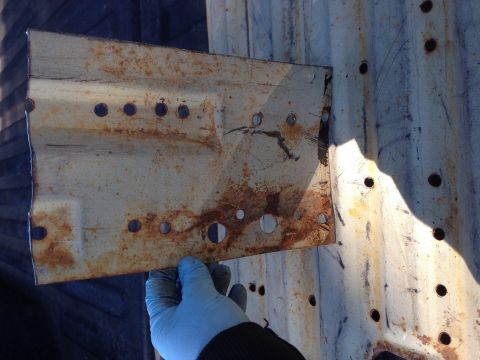 1979 Ford Bronco - A heavily rusted metal bracket, likely a vehicle part, is held up for inspection against a corrugated surface.