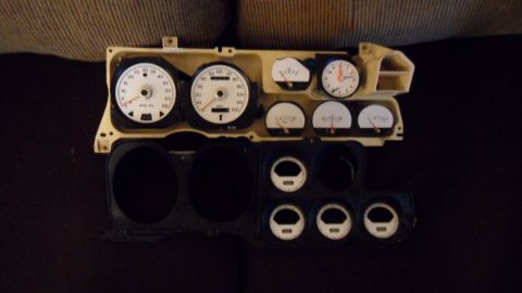 1972 Ford Ranchero - A collection of car gauges, including a speedometer, tachometer, clock, and auxiliary gauges, are laid out on a dark surface.