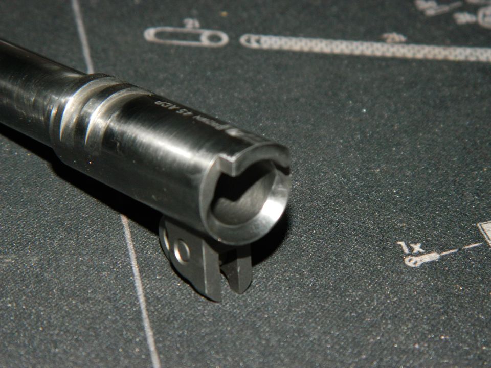 Close-up of a gun barrel with "9mm 45 ACP" visible. It rests on a mat with diagrams