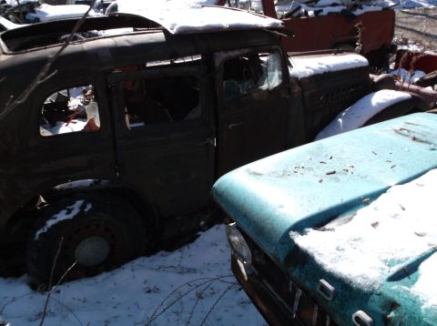 1974 Dodge Challenger - An old, damaged sedan sits in a junkyard covered in snow, with another vehicle partially visible in the foreground.