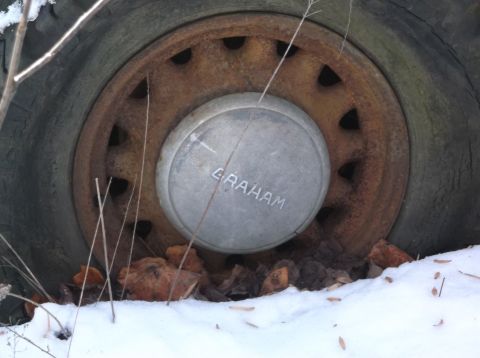 1974 Dodge Challenger - Close-up of a rusty wheel a GRAHAM branded hubcap, partially covered in snow and fallen leaves.