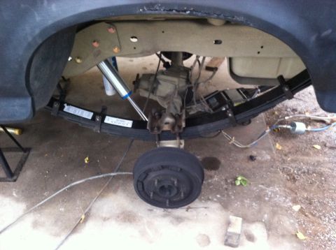1995 Ford Bronco - Undercarriage view of a vehicle's rear axle and suspension system, showing leaf springs and a shock absorber.