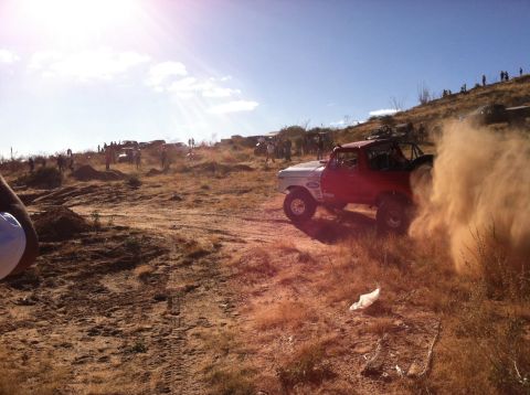 1995 Ford Bronco - A Ford Bronco races off-road, creating a large dust cloud. Multiple vehicles and spectators are visible.