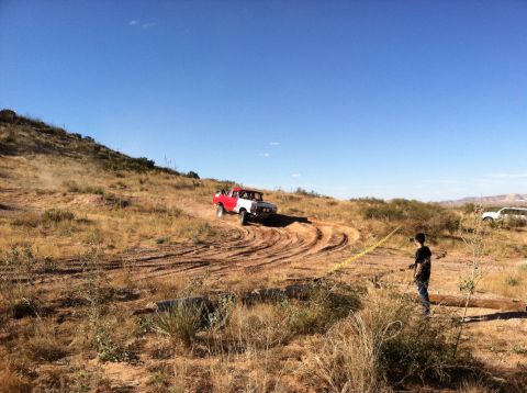1995 Ford Bronco - A red and white Ford Bronco navigates a dry, hilly terrain with a person observing nearby.