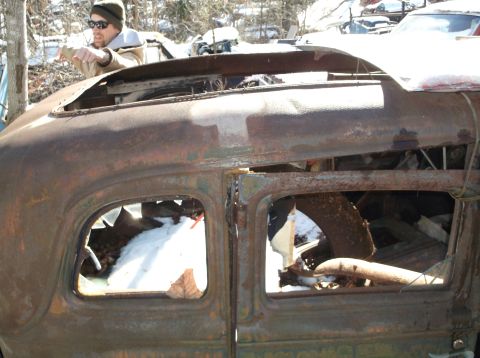 1974 Dodge Challenger - A person points towards the interior of a heavily rusted vehicle, with snow visible through the broken windows.