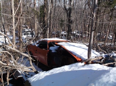 1974 Dodge Challenger - An old orange car sits abandoned in a snowy junkyard, partially obscured by fallen branches and snow.