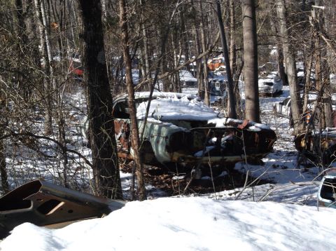 1974 Dodge Challenger - Multiple derelict vehicles sit abandoned in a snowy wooded area, their bodies showing significant rust and decay.