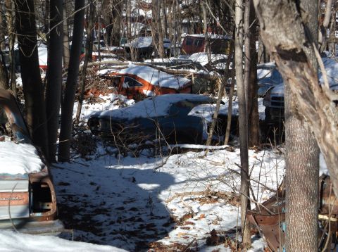 1974 Dodge Challenger - Multiple abandoned vehicles sit in a snowy junkyard during winter.