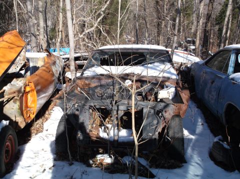 1974 Dodge Challenger - A derelict muscle car sits in a snowy junkyard, its front end heavily rusted and exposed.