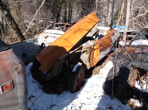 1974 Dodge Challenger - Junkyard scene with a damaged orange car hood and door visible amongst other derelict vehicles in the snow.