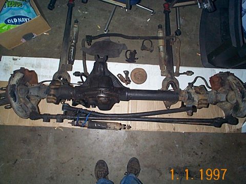 1981 Ford Bronco - A disassembled Dana 44 front axle assembly is laid out on the floor, showing the differential, brake components, and suspension parts.