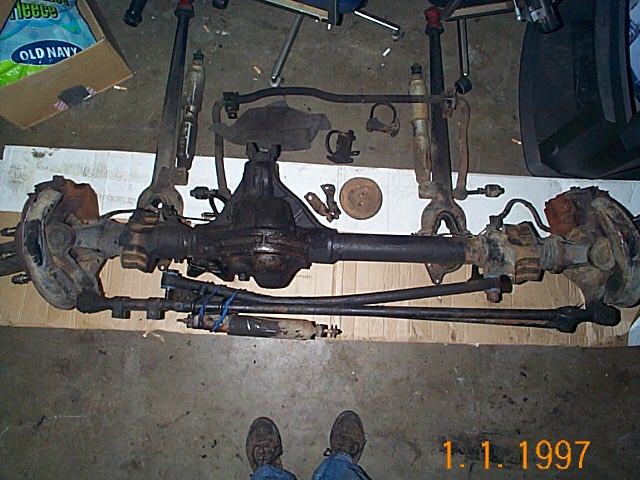 Disassembled solid front axle with differential, tie rod and radius arms on garage floor
